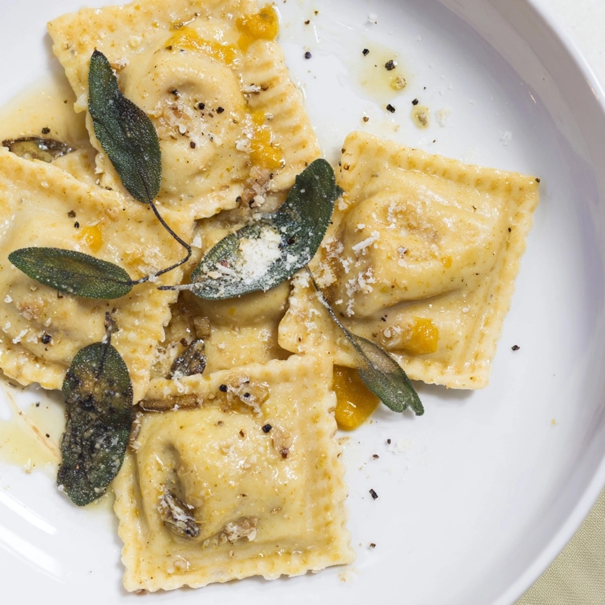 Golden Sage Butter Pumpkin Ravioli glistens, speckled with parmesan and vibrant green sage.