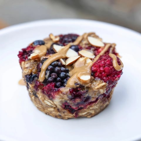 Golden-baked oatmeal cups with juicy winter berries and a swirl of creamy almond butter, ready to eat.