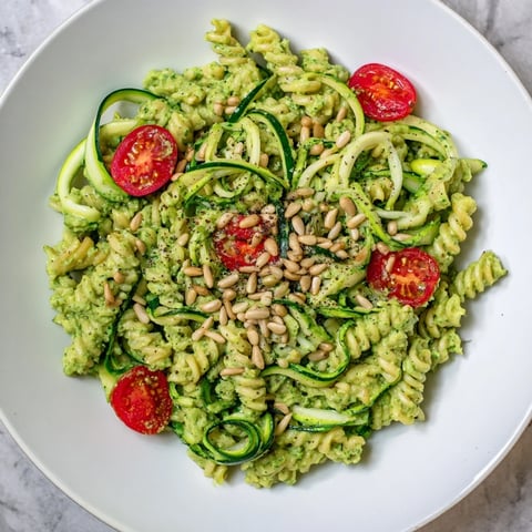 Creamy vegan green goddess pasta, coated in vibrant green sauce, plated with fresh tomatoes.