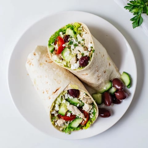 Freshly assembled Greek Lemon Chicken Salad Wrap with vibrant greens, Kalamata olives, and a lemony dressing, served on a platter.