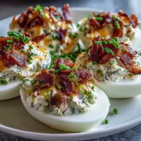 Spicy jalapeño popper deviled eggs with creamy cheese and bacon, topped with fresh jalapeño slices for a bold appetizer.  
